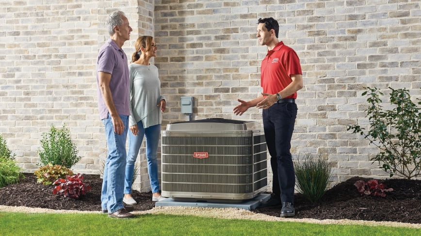 Technician explaining Bryant air conditioner system to homeowners outside their Grand Rapids home